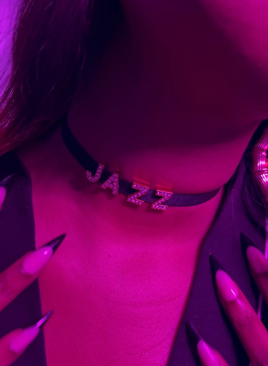 Necklace with 'JAZZ' pendant on a person's neck, with a pinkish-purple filter.